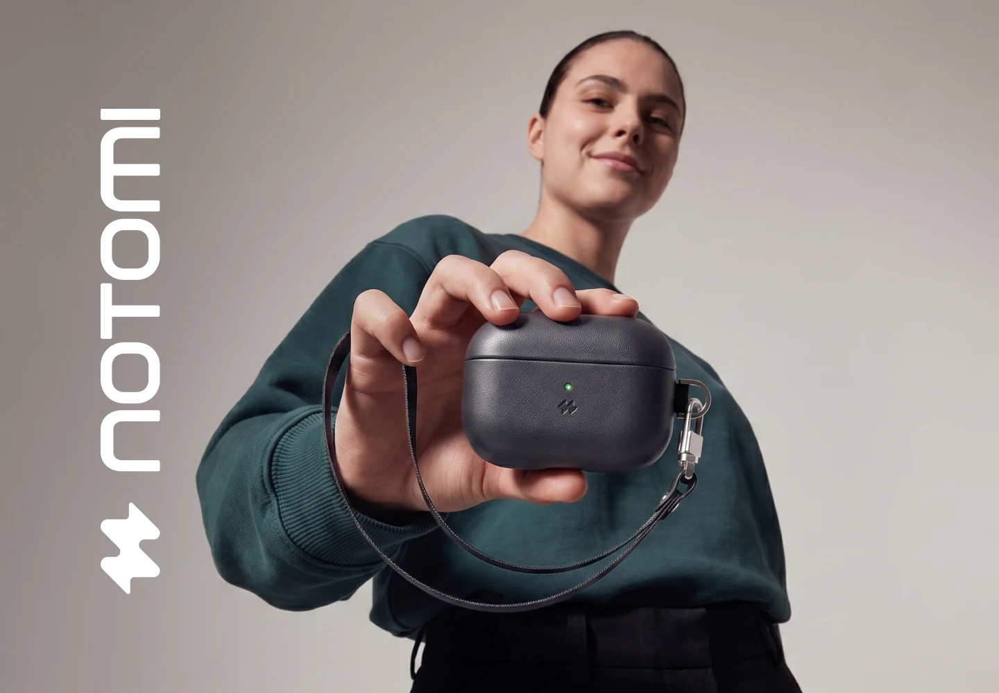 Kobieta prezentuje pomarańczowe etui Notomi ze skóry naturalnej do AirPods 5 / 4, z paskiem i karabińczykiem.