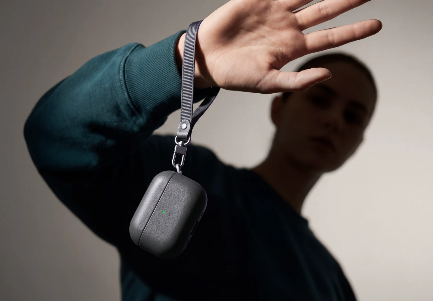 Kobieta trzyma pomarańczowe etui Notomi ze skóry naturalnej do AirPods 5 / 4 na pasku założonym na nadgarstek.