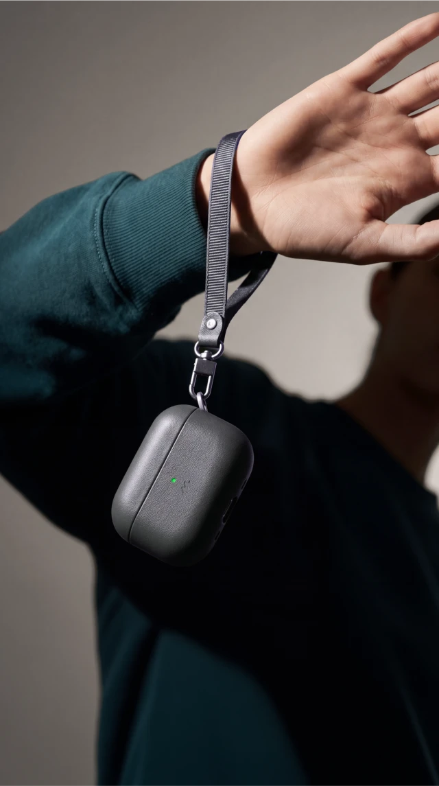 Kobieta trzyma pomarańczowe etui Notomi ze skóry naturalnej do AirPods 5 / 4 na pasku założonym na nadgarstek.