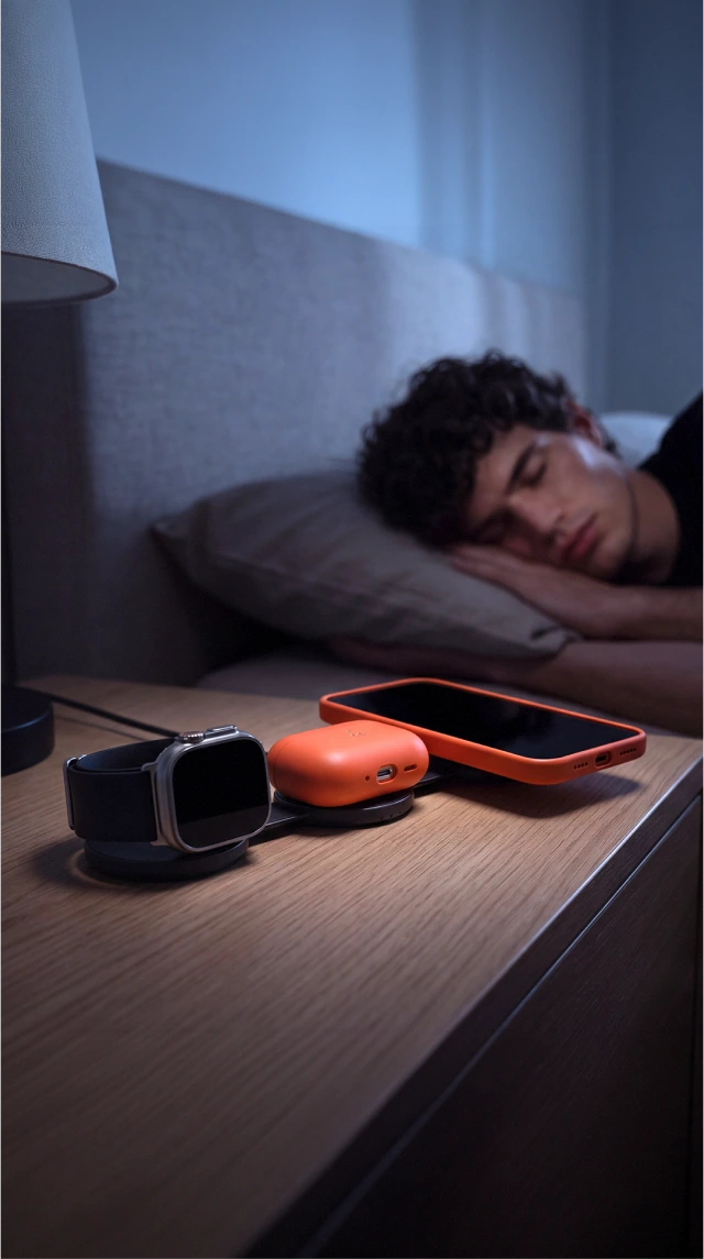Biała, składana mini ładowarka indukcyjna 15 W Noto Charge Pad Go ładuje iPhone’a, Apple Watch i AirPods na stoliku obok łóżka.