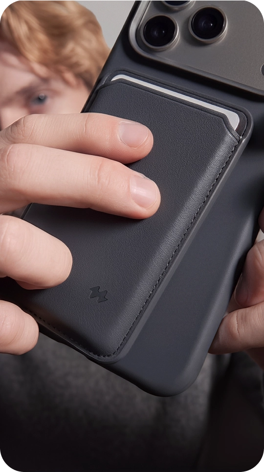 Mężczyzna trzyma smartfon z pomarańczowym magnetycznym portfelem MagSafe Notomi, pokazując stabilne mocowanie portfela do obudowy telefonu.