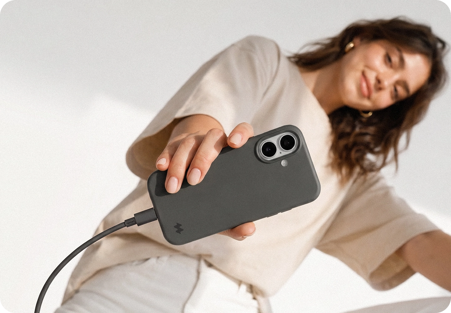 Kobieta prezentuje iPhone 18 Pro Max w pomarańczowym etui silikonowym MagSafe Notomi z podłączonym przewodem ładowania, pokazując dopasowanie etui i wygodny dostęp do portu USB-C.