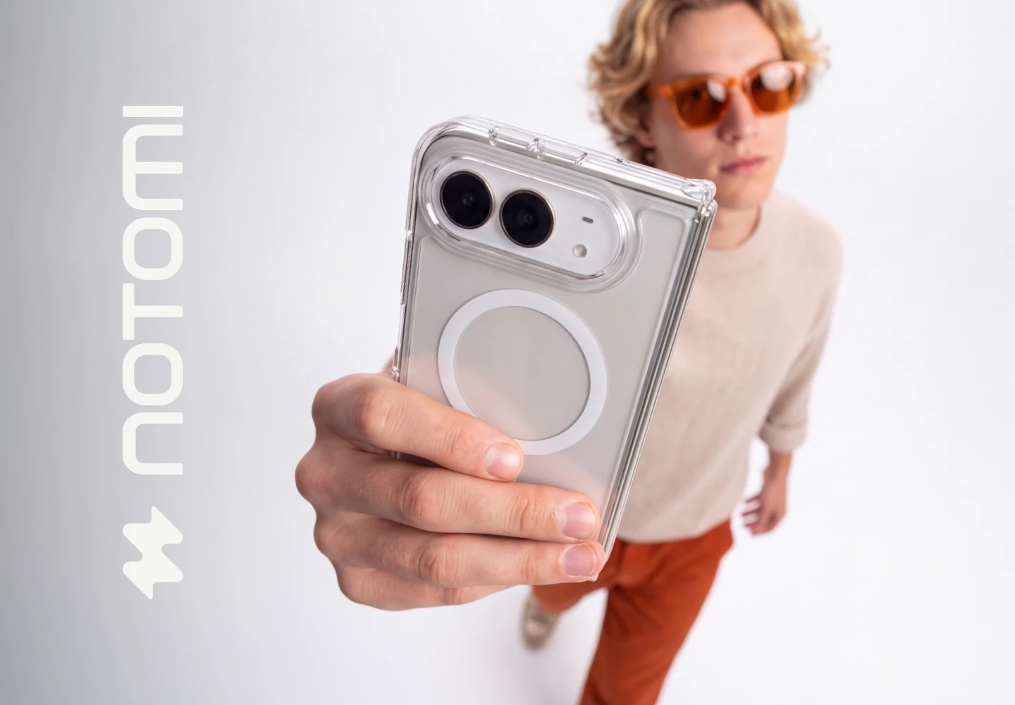 Młody mężczyzna trzyma iPhone Duo w transparentnym etui Clear MagSafe Notomi, prezentując minimalistyczne wykończenie, dopasowanie do telefonu i elegancki design akcesorium.