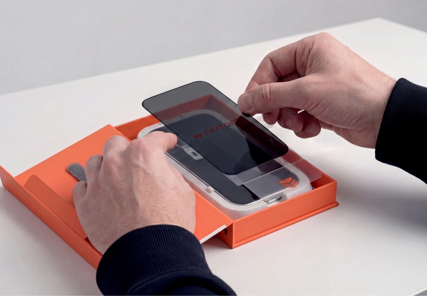Dłonie montują prywatyzujące szkło hartowane Notomi 9H na iPhone 18 Pro Max z ekologicznym, papierowym aplikatorem.