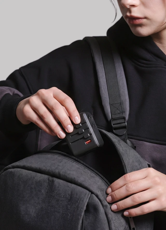 Kobieta wkłada kompaktowy, biały adapter podróżny Notomi GaN 65 W do plecaka.